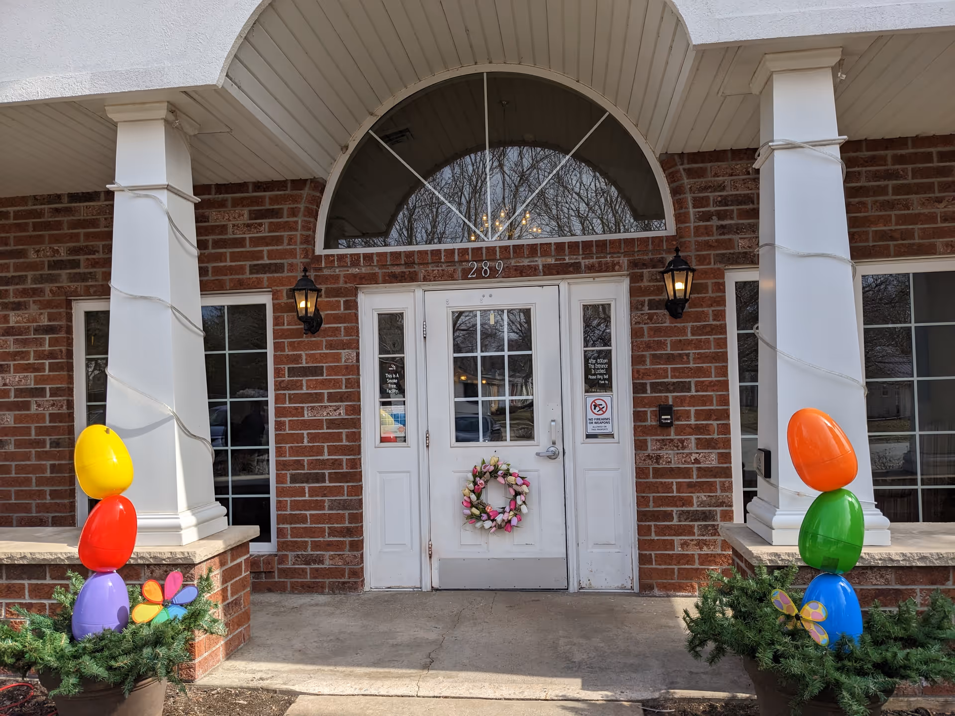 Front entrance of a brick senior living facility with wreath, balloons, and lanterns.