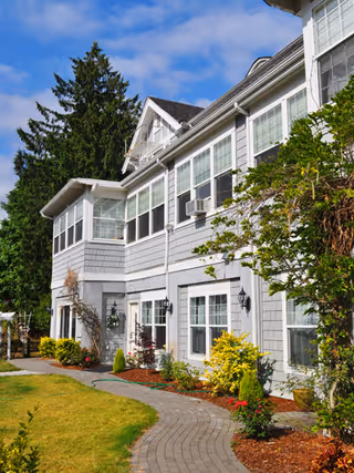 Two-story gray Shumway Mansion II exterior with manicured lawn and curved stone walkway.