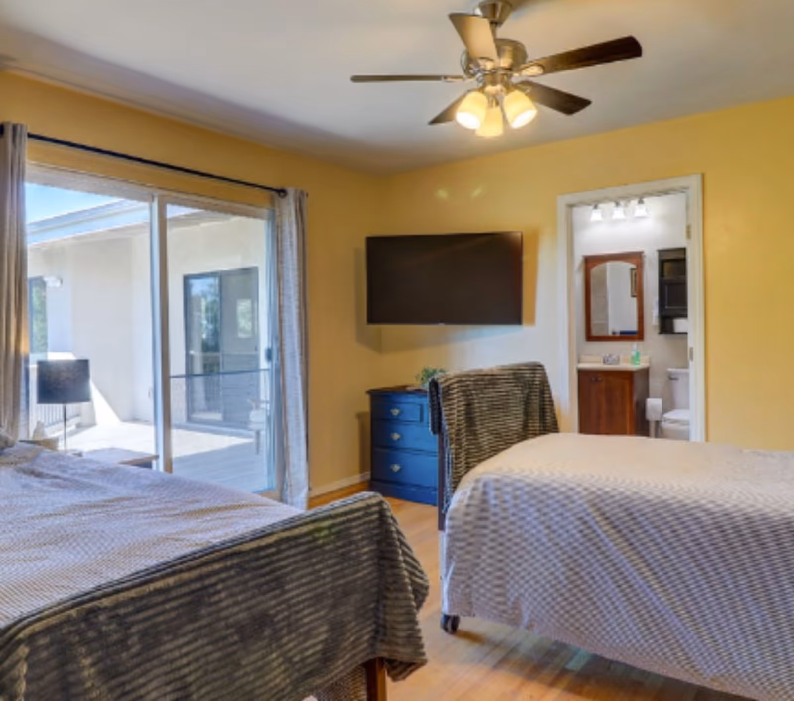 Two beds in a bright yellow bedroom with a sliding door to patio and TV.