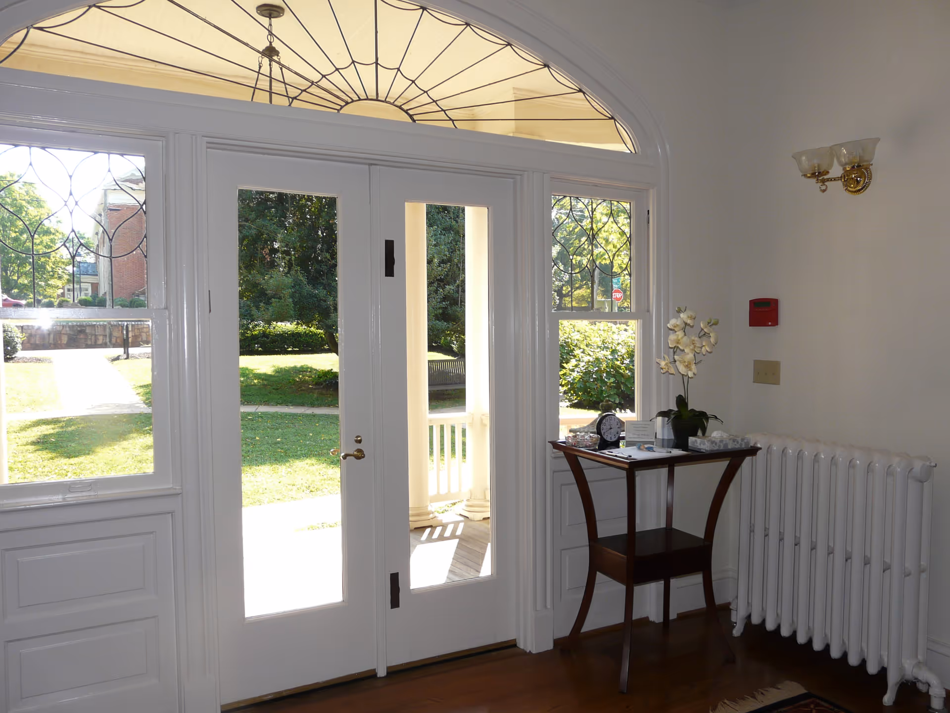 Bright interior entry with glass doors, arched window, and a small table with orchid.