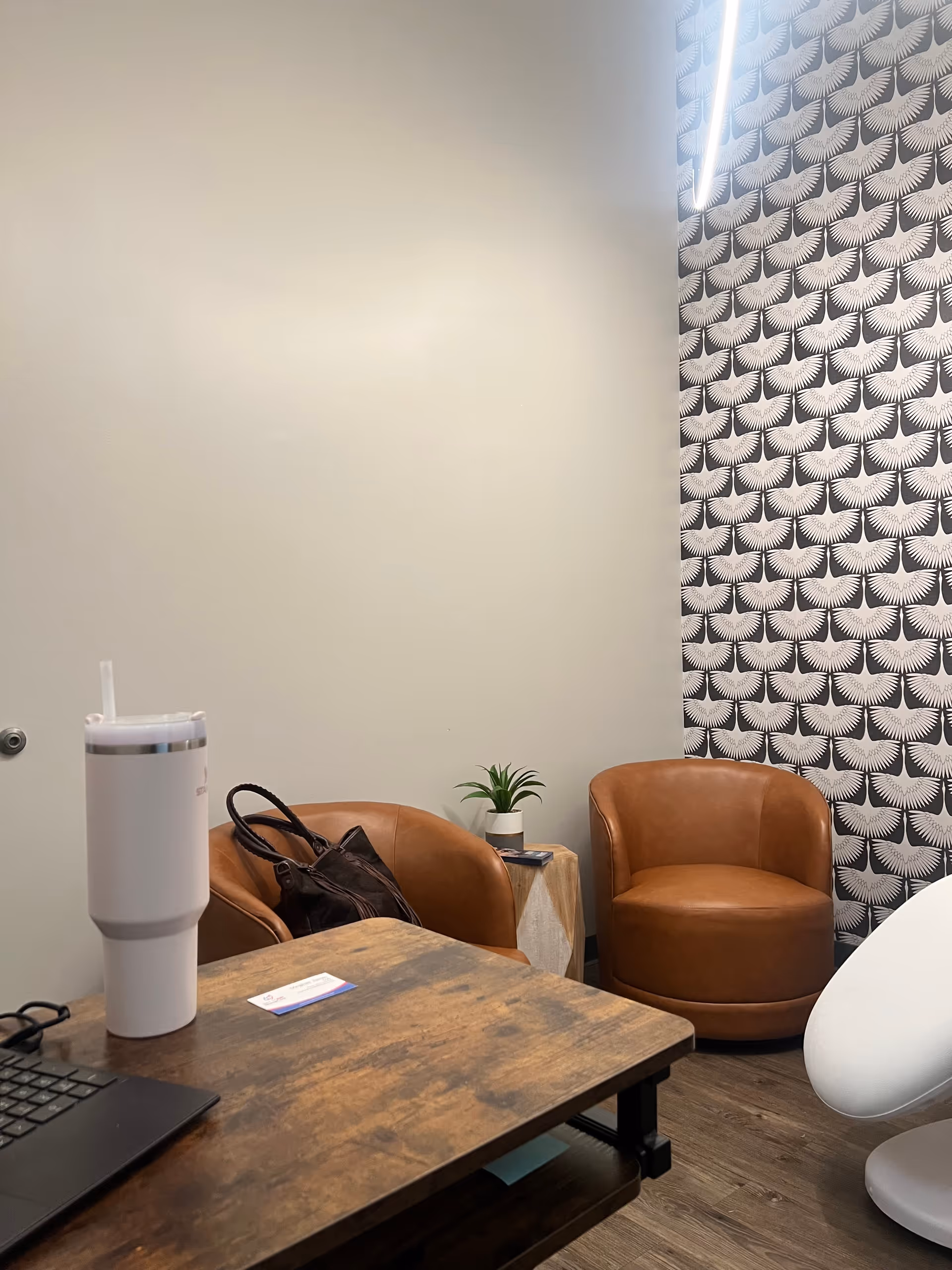 A small interior office lounge with brown leather chairs, a wooden desk, and patterned wallpaper.