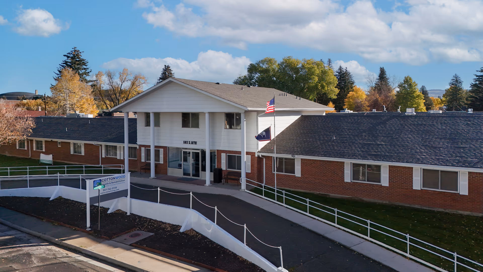 A single-story brick senior living facility with a central entrance and flags.