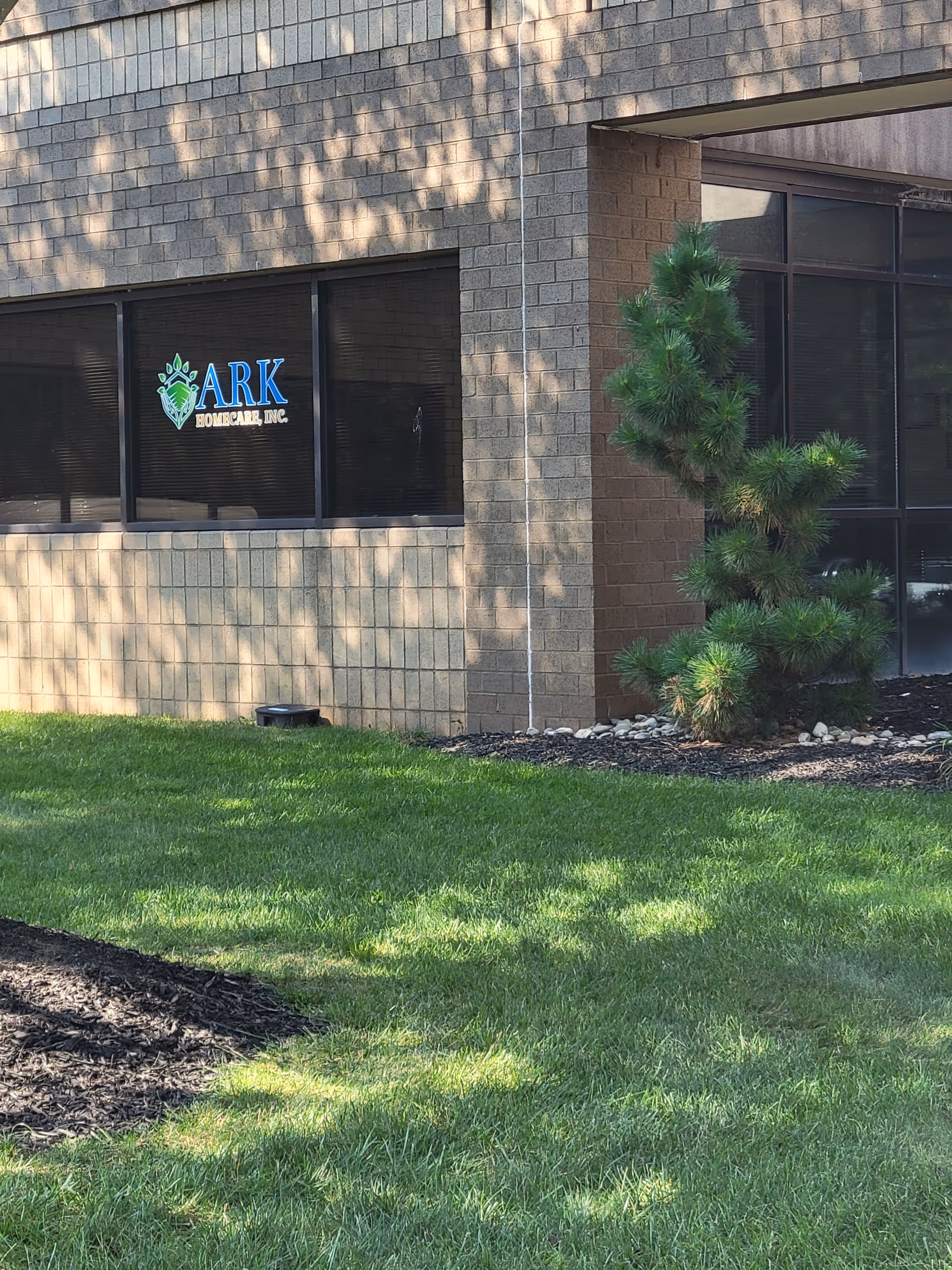 Exterior view of Ark HomeCare, Inc. facility with sign on window and landscaping.