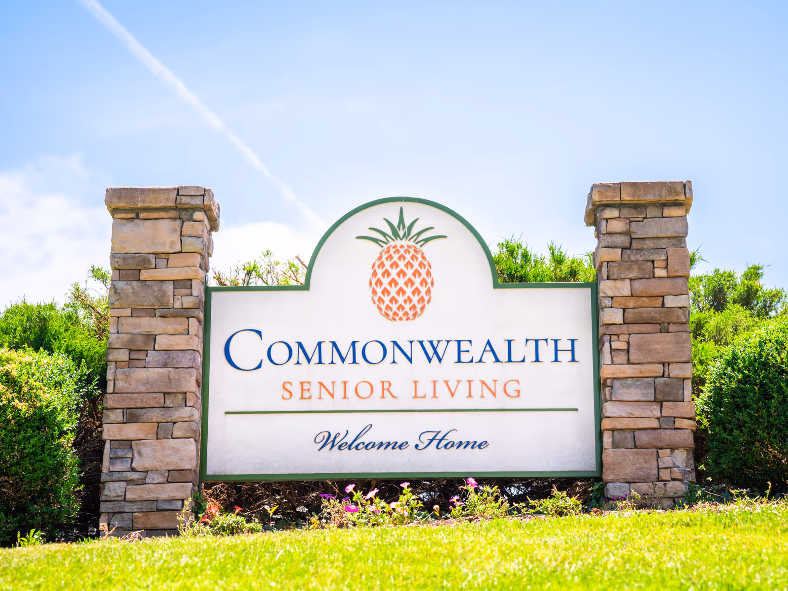 Front entrance sign reads Commonwealth Senior Living with pineapple logo, flanked by stone columns.