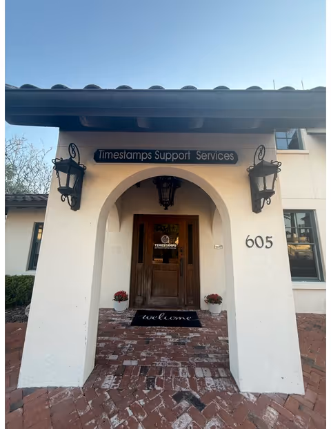 Arched front entrance of a white building with wooden door and welcome mat.
