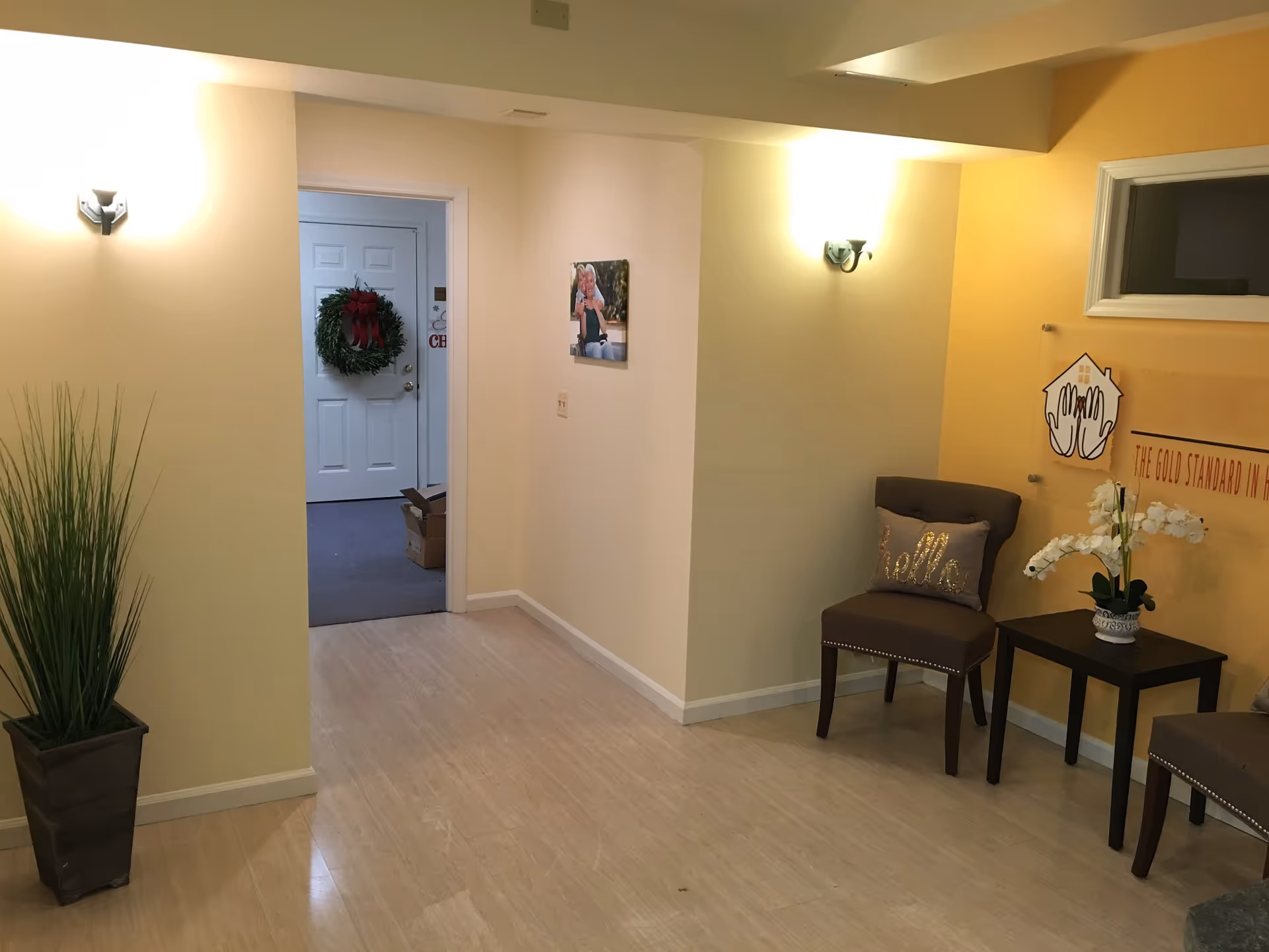 Hallway of a senior living facility with chairs, plants, and a wreath on a door.