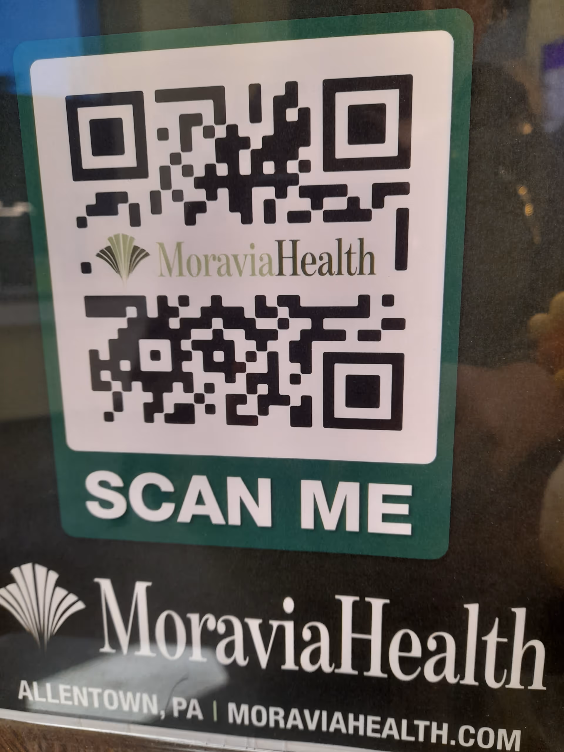 QR code sticker on a glass door featuring Moravia Health Allentown branding; scan me.