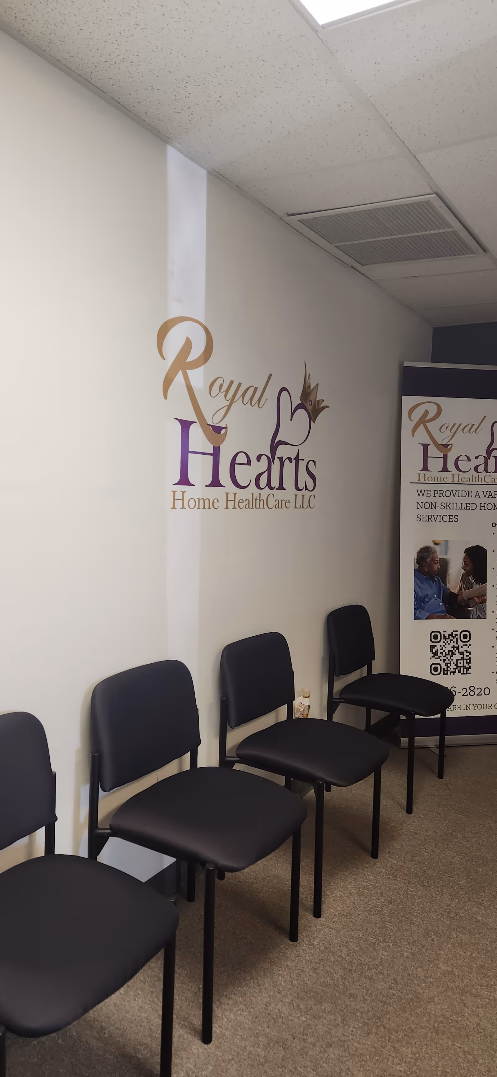 Row of black chairs along a wall with a Royal Hearts banner in a waiting area.