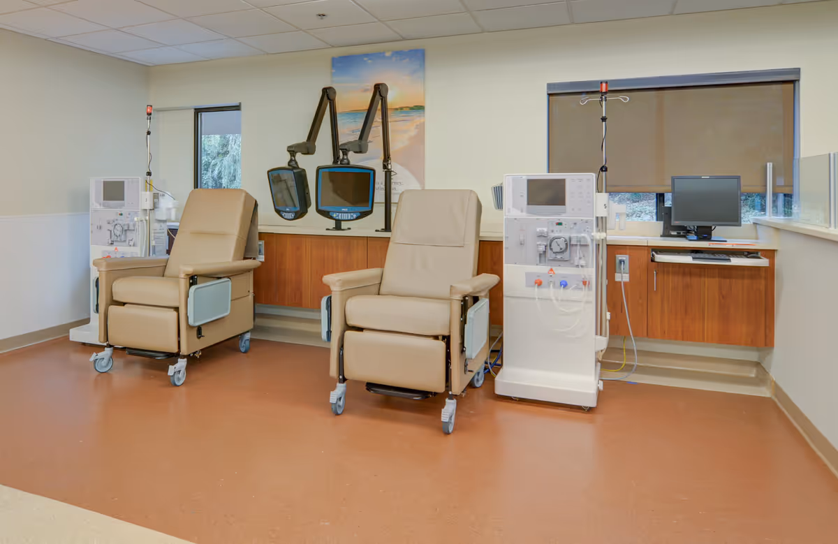 Two beige recliner chairs with medical dialysis machines and a computer workstation in a clinical room.