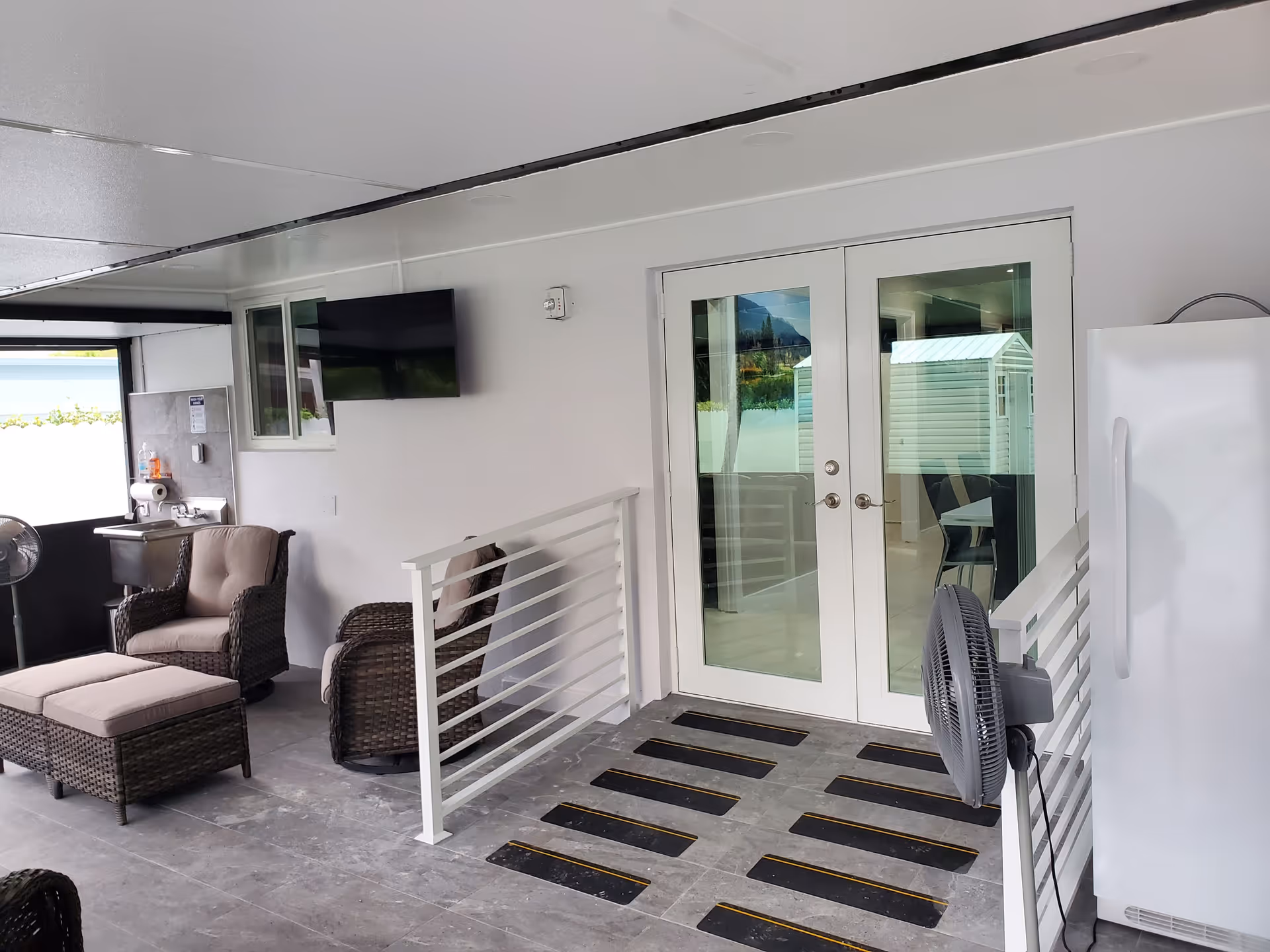 Covered outdoor lounge area with wicker furniture, fans, and glass doors.