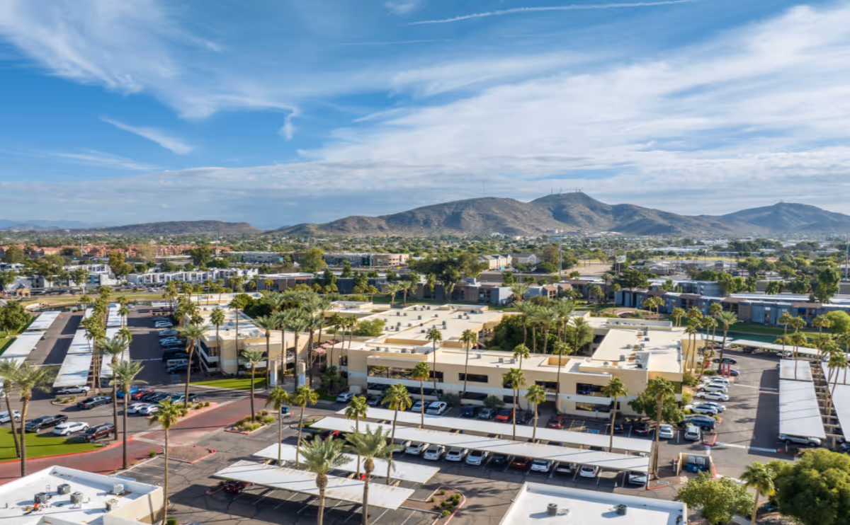 Aerial view of a senior living campus with parking lots, palm trees, and distant hills.