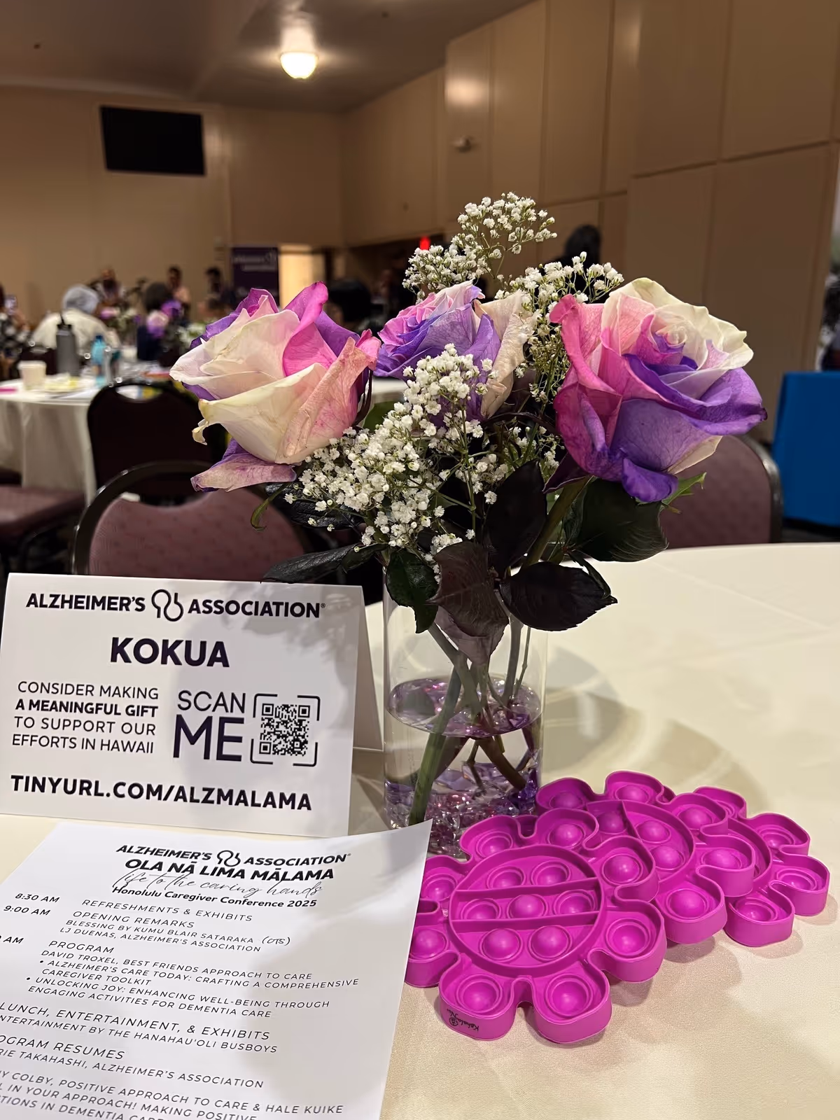Table with a floral centerpiece and Alzheimer's Association sign at an indoor event.
