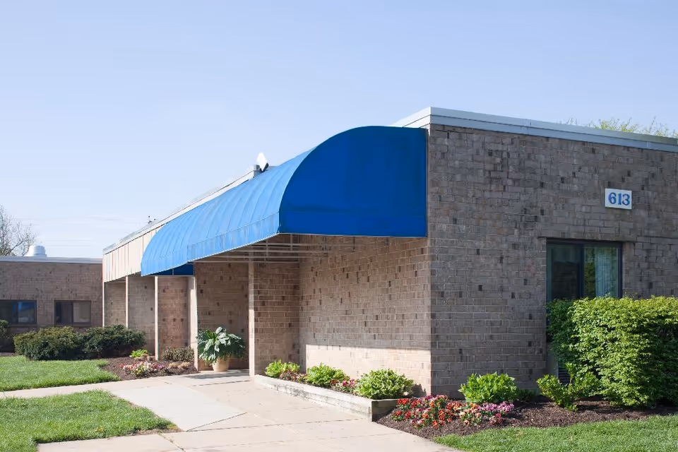 Brick senior living facility exterior with a bright blue curved awning over the entrance.