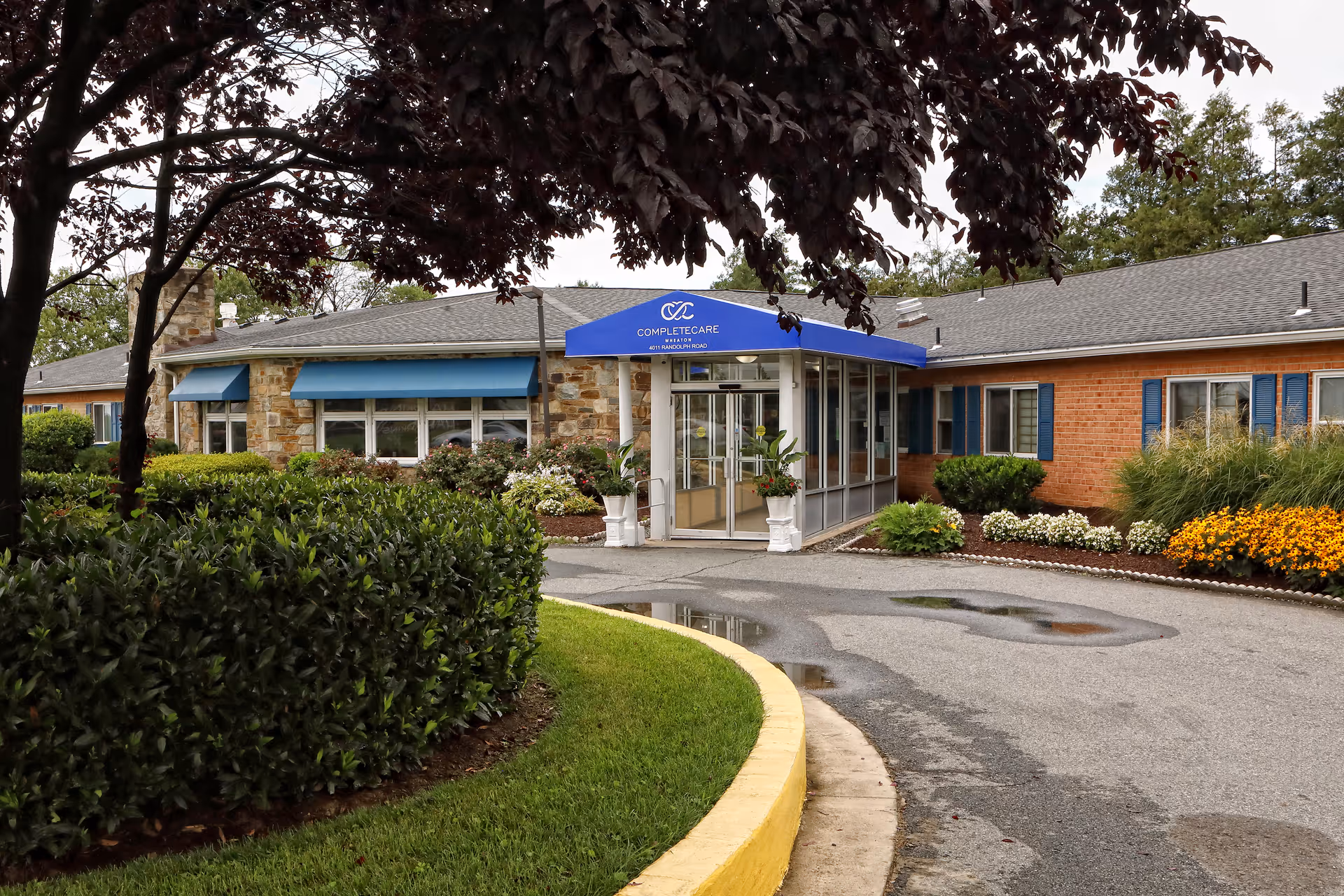 Exterior view of Complete Care at Wheaton with glass entrance and landscaped surroundings.