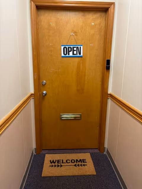 Wooden interior hallway door with OPEN sign and welcome mat in a senior facility.