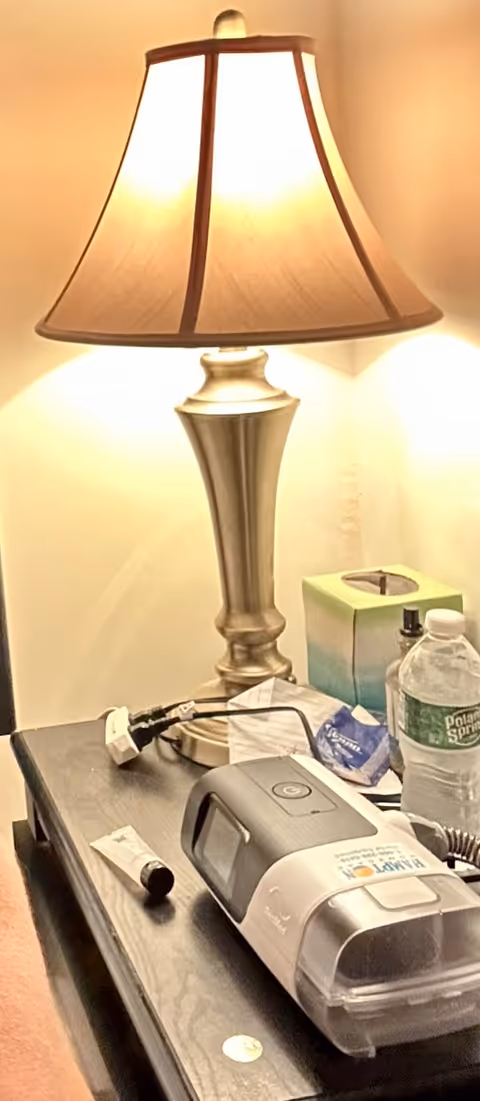 A bedside table with a lamp, water bottle, tissues, and a medical device.