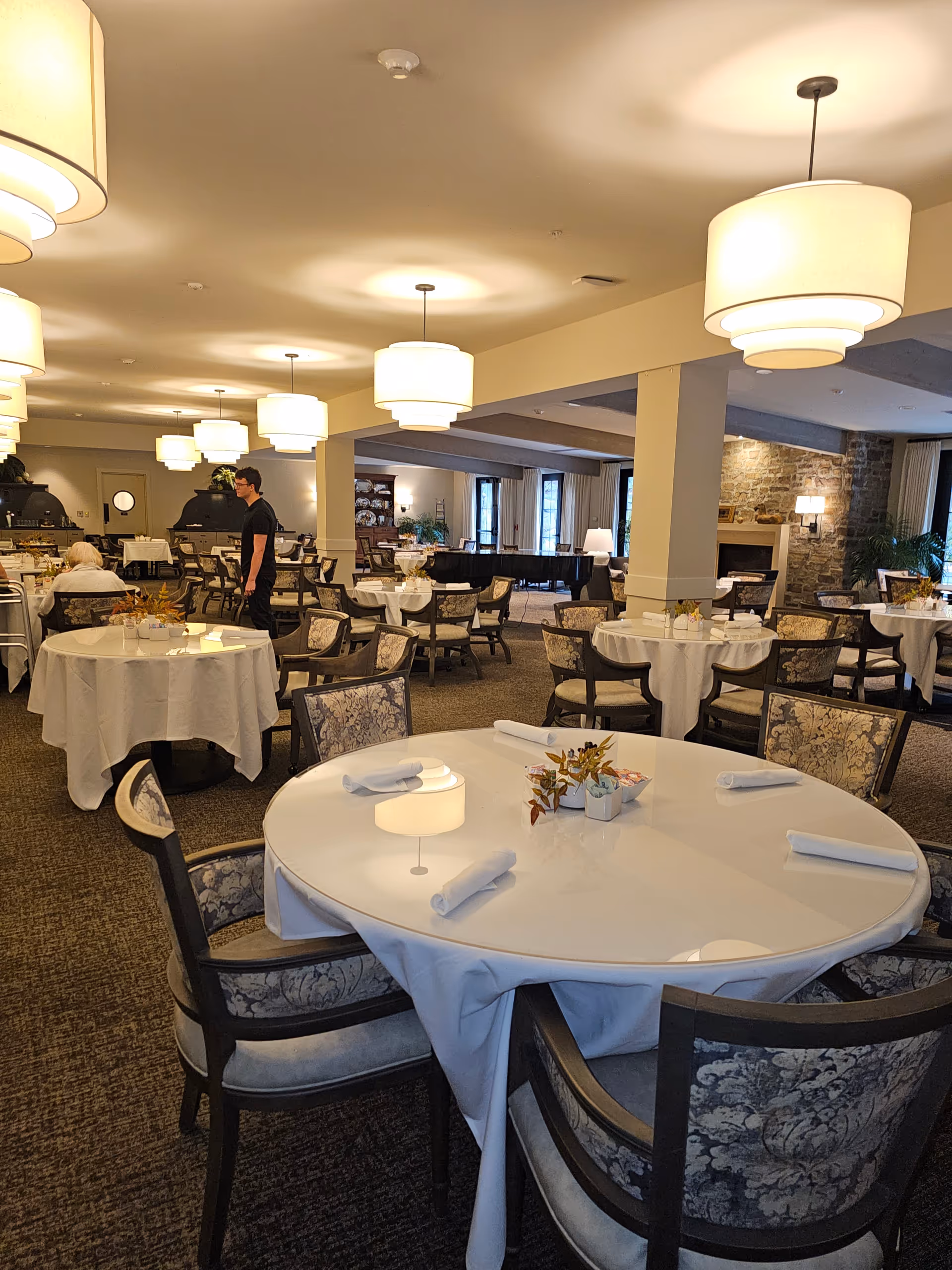 Elegant dining room with round tables set with white linens beneath warm pendant lighting.