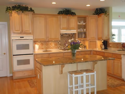 Bright wooden kitchen with island, granite countertop, and built in ovens in a senior living facility.