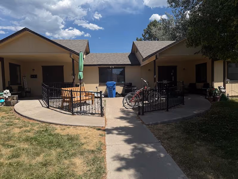 Outdoor courtyard of Pocatello Assisted Living Center with a curved concrete path, benches, bikes, and shade.