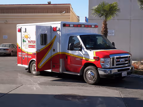 Red and white ambulance parked outside a facility with palm tree in background.