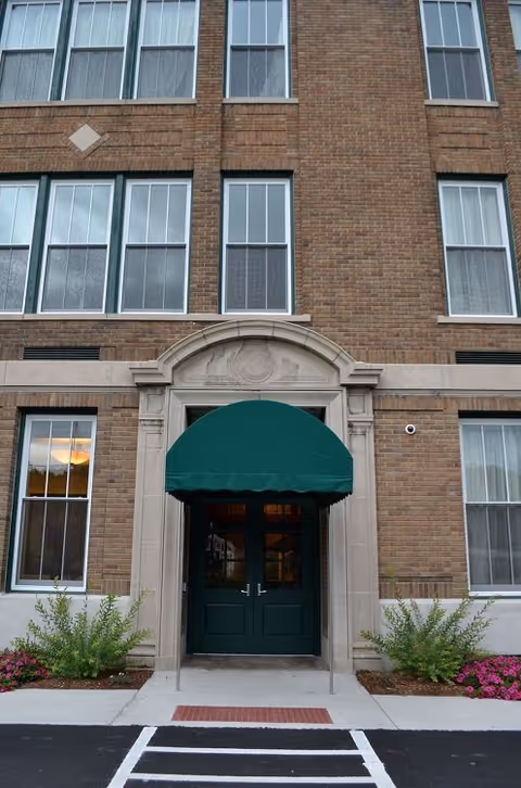 Brick senior living facility entrance with green canopy over double doors.