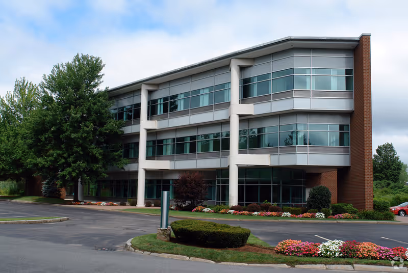 Modern three-story senior living facility with glass windows and landscaped surroundings.
