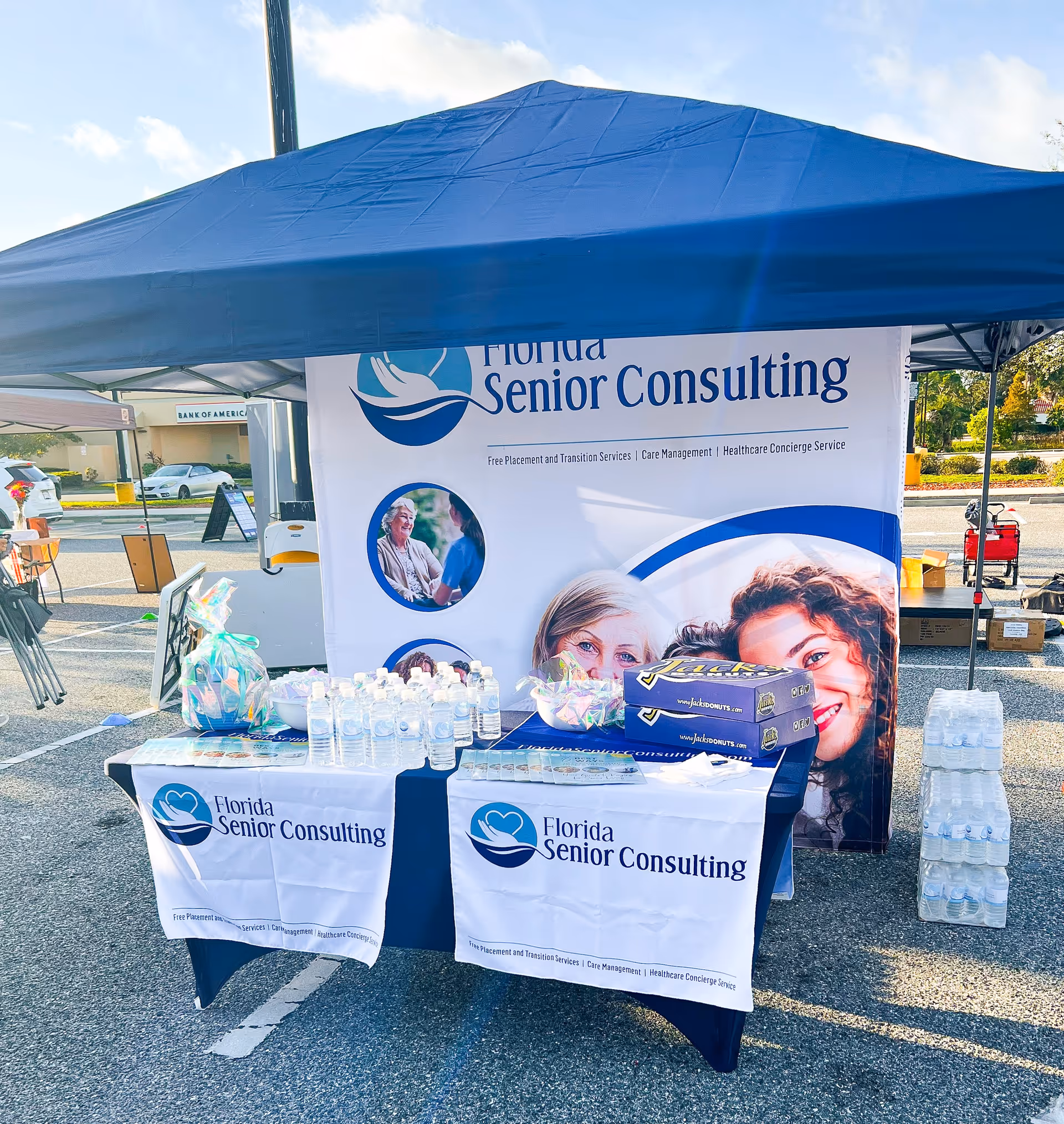 Outdoor booth for Florida Senior Consulting with banners, tables, water bottles in a parking lot.