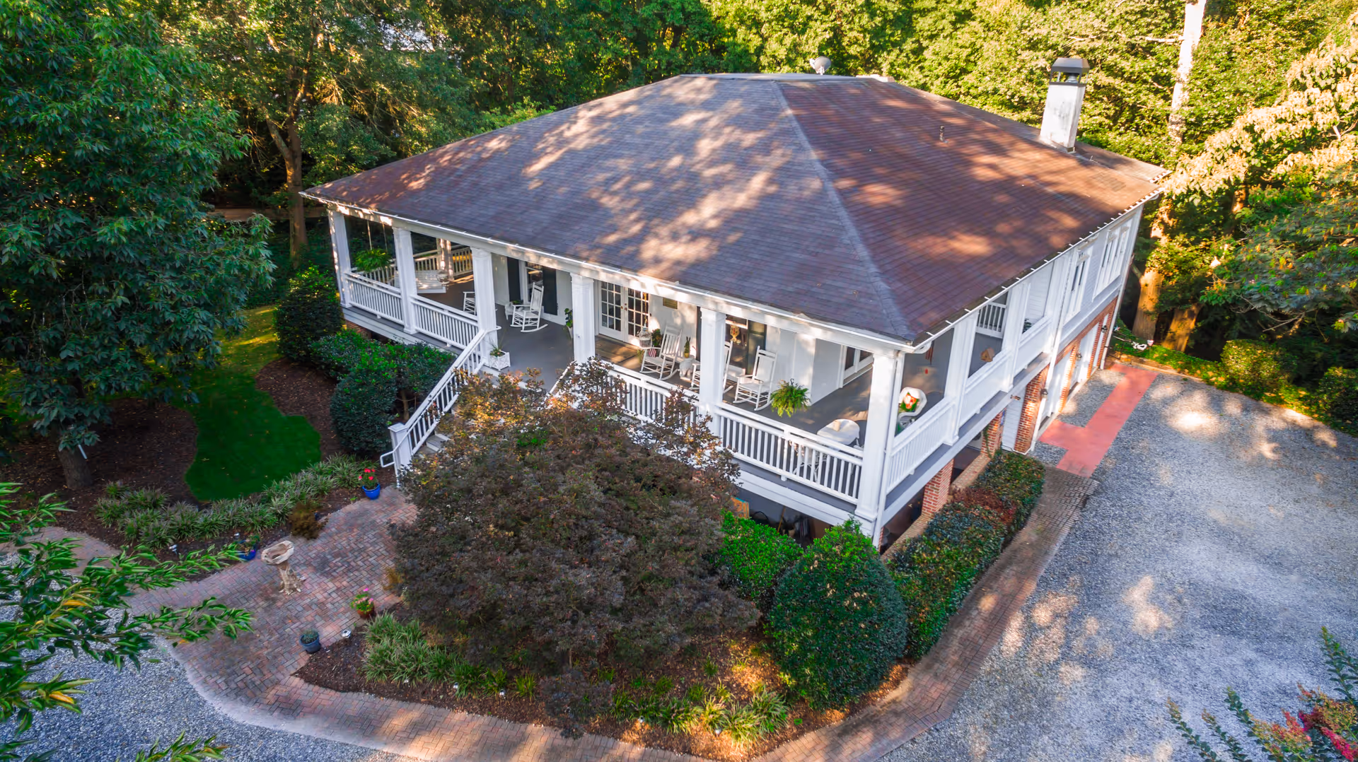 A white house with a wraparound porch, surrounded by trees, photographed from above.