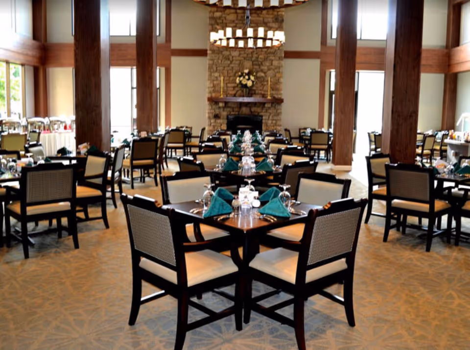 Spacious dining room with multiple set tables and a stone fireplace at the far end.