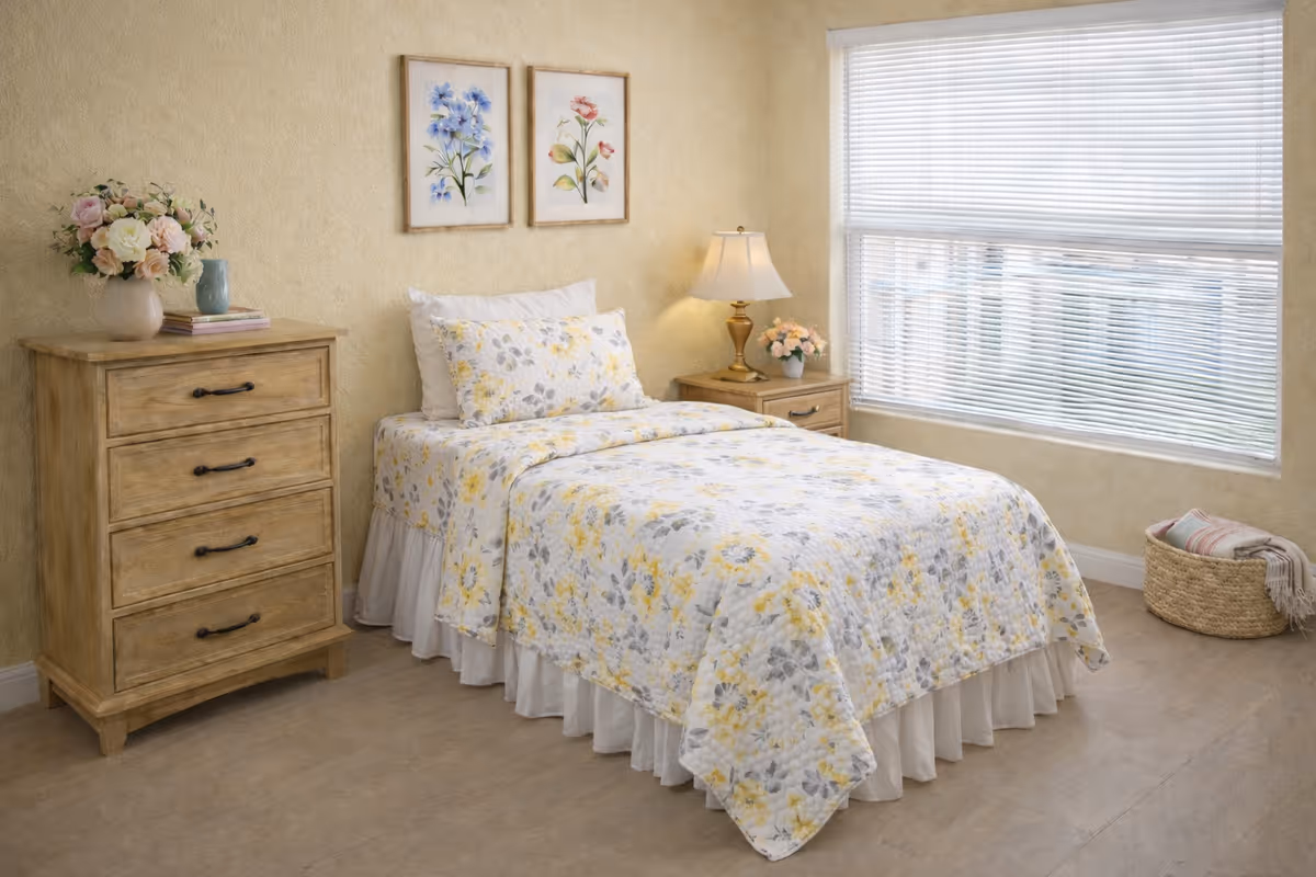 Cozy bedroom featuring floral bedding, wooden dresser, nightstand, lamp, and a large window.