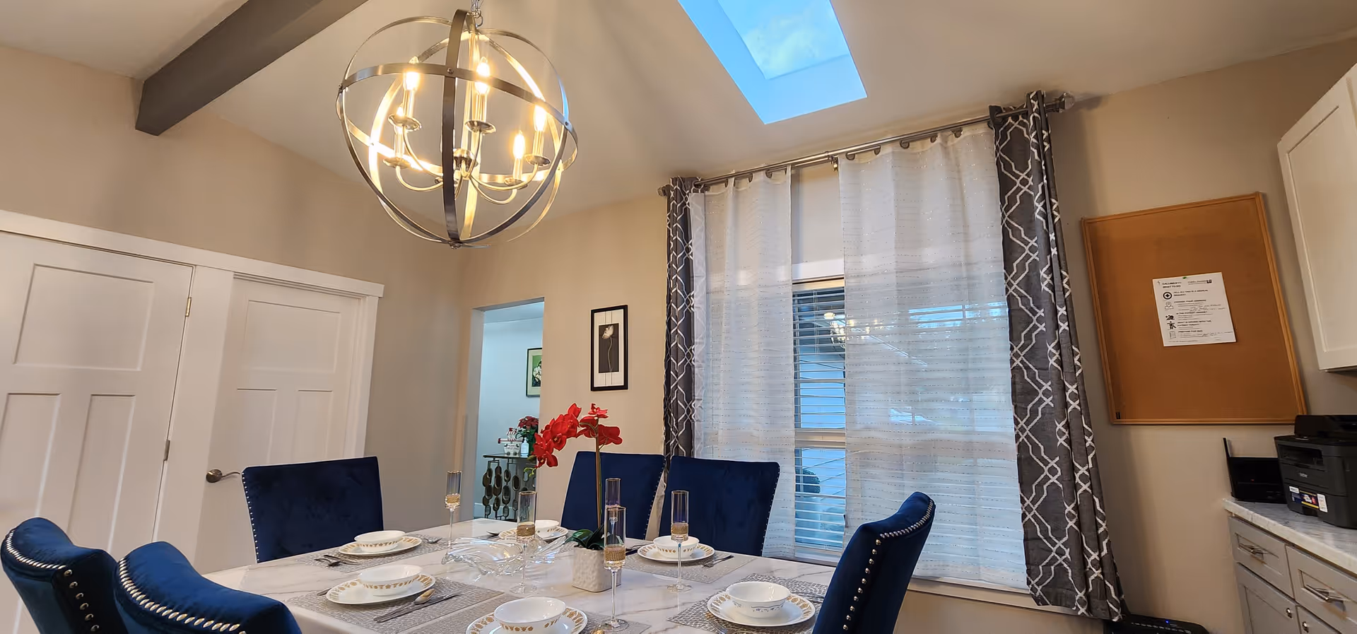 A bright dining room with a chandelier, blue upholstered chairs, and a table set for meals.