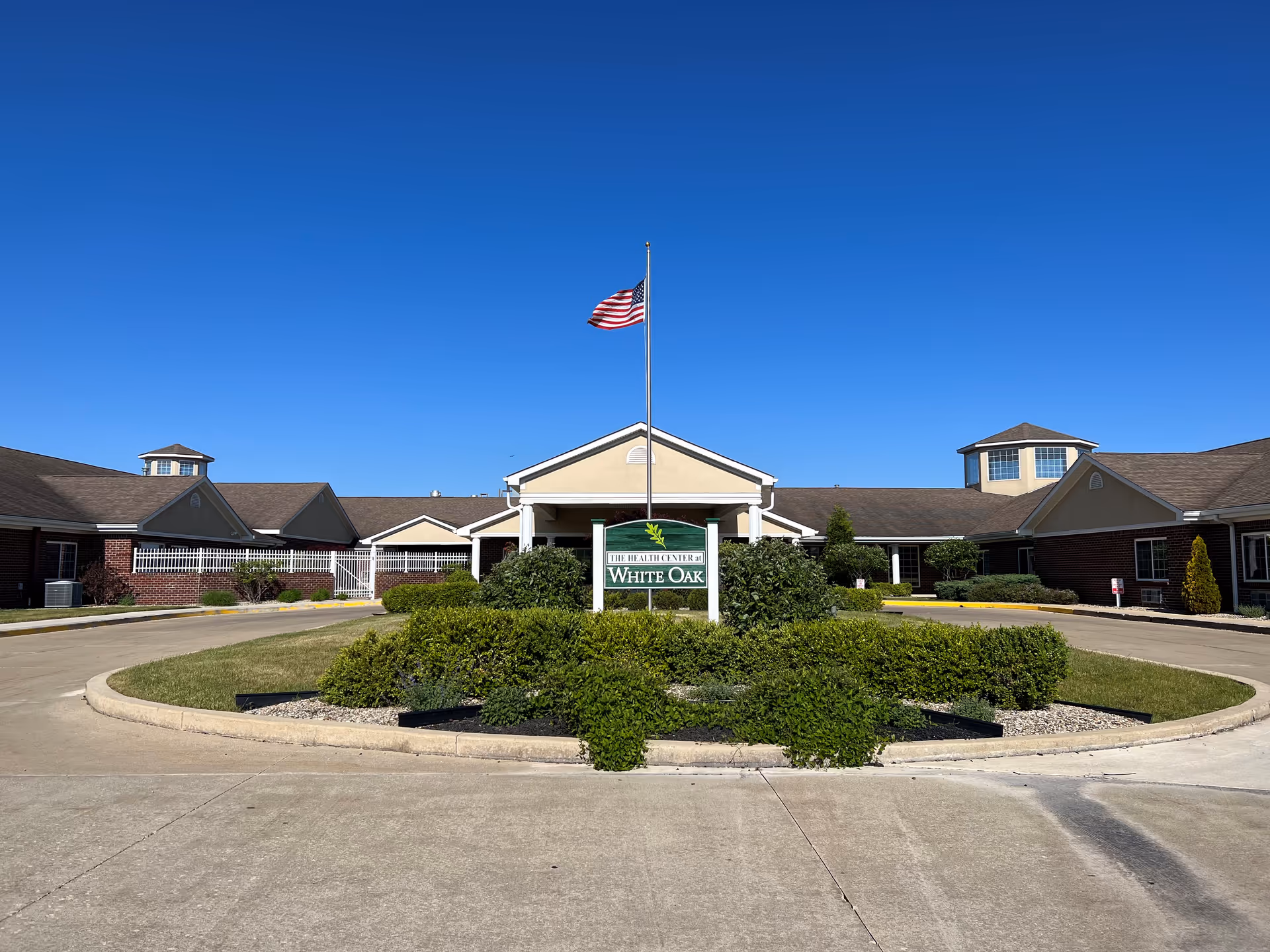Front view of White Oak Health Campus with circular drive, shrubs, and American flag