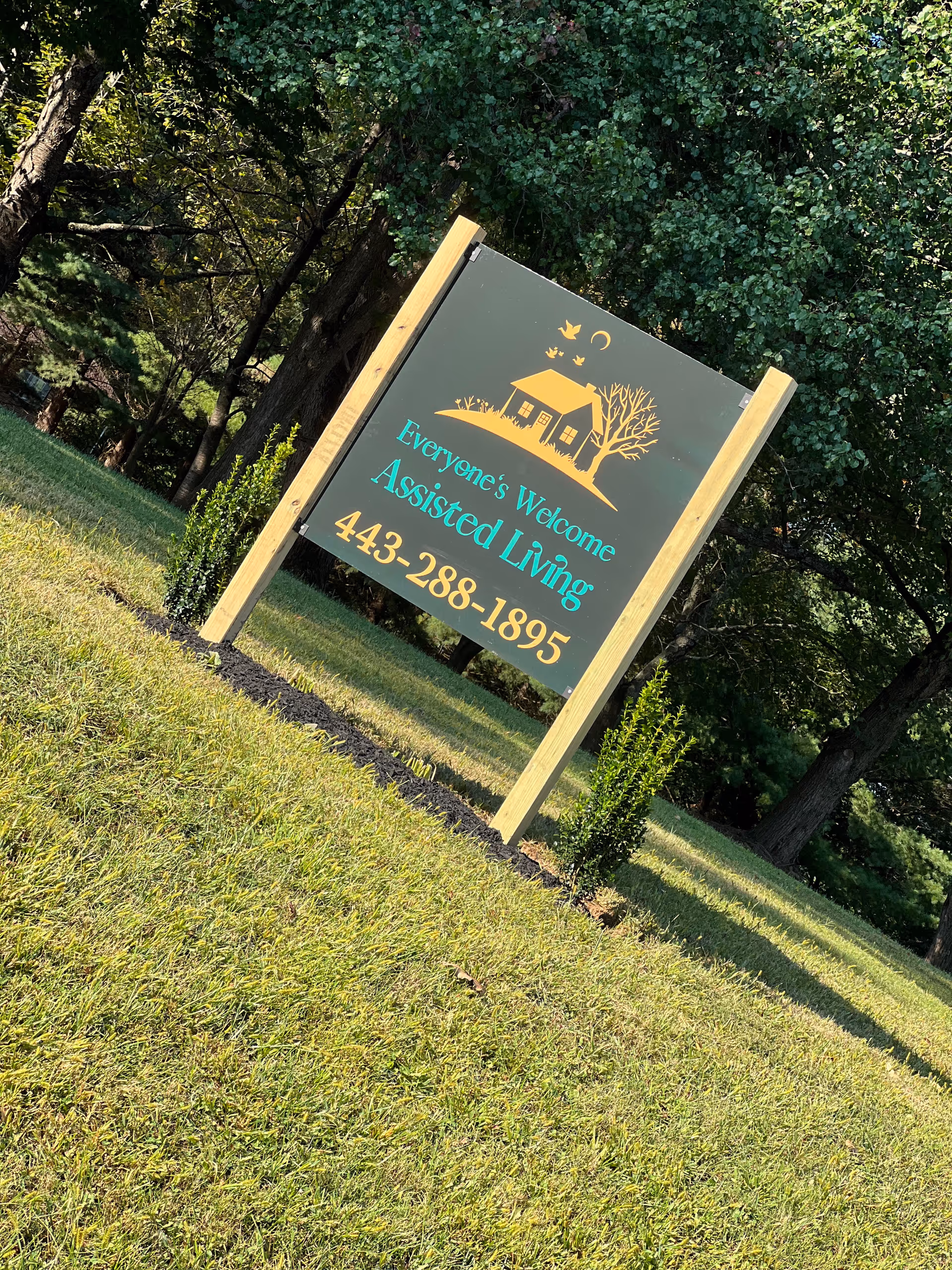 Outdoor sign for Everyone's Welcome Assisted Living on a grassy lawn with trees.
