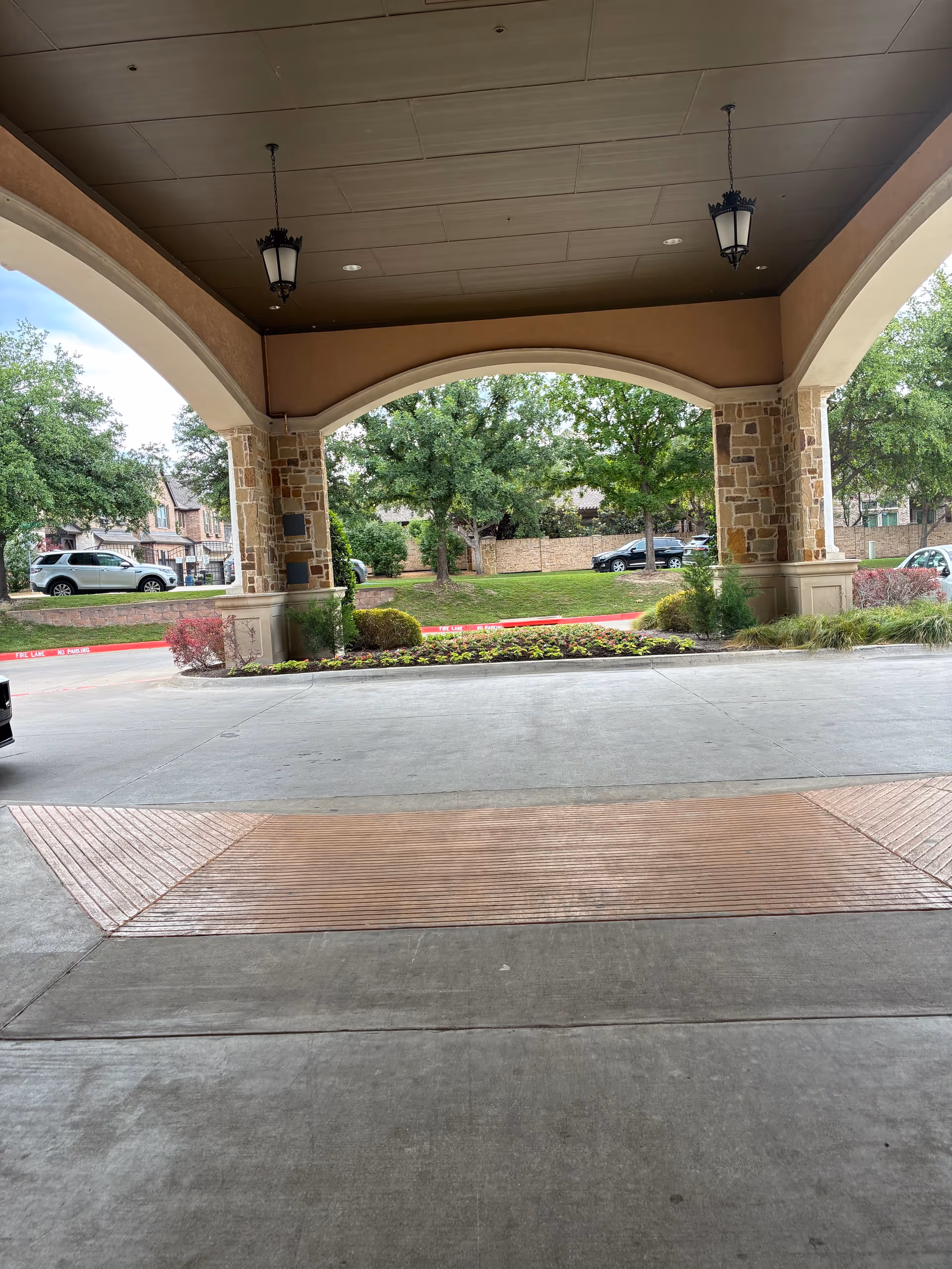 Covered arched entrance to a senior living facility with stone columns and landscaping.
