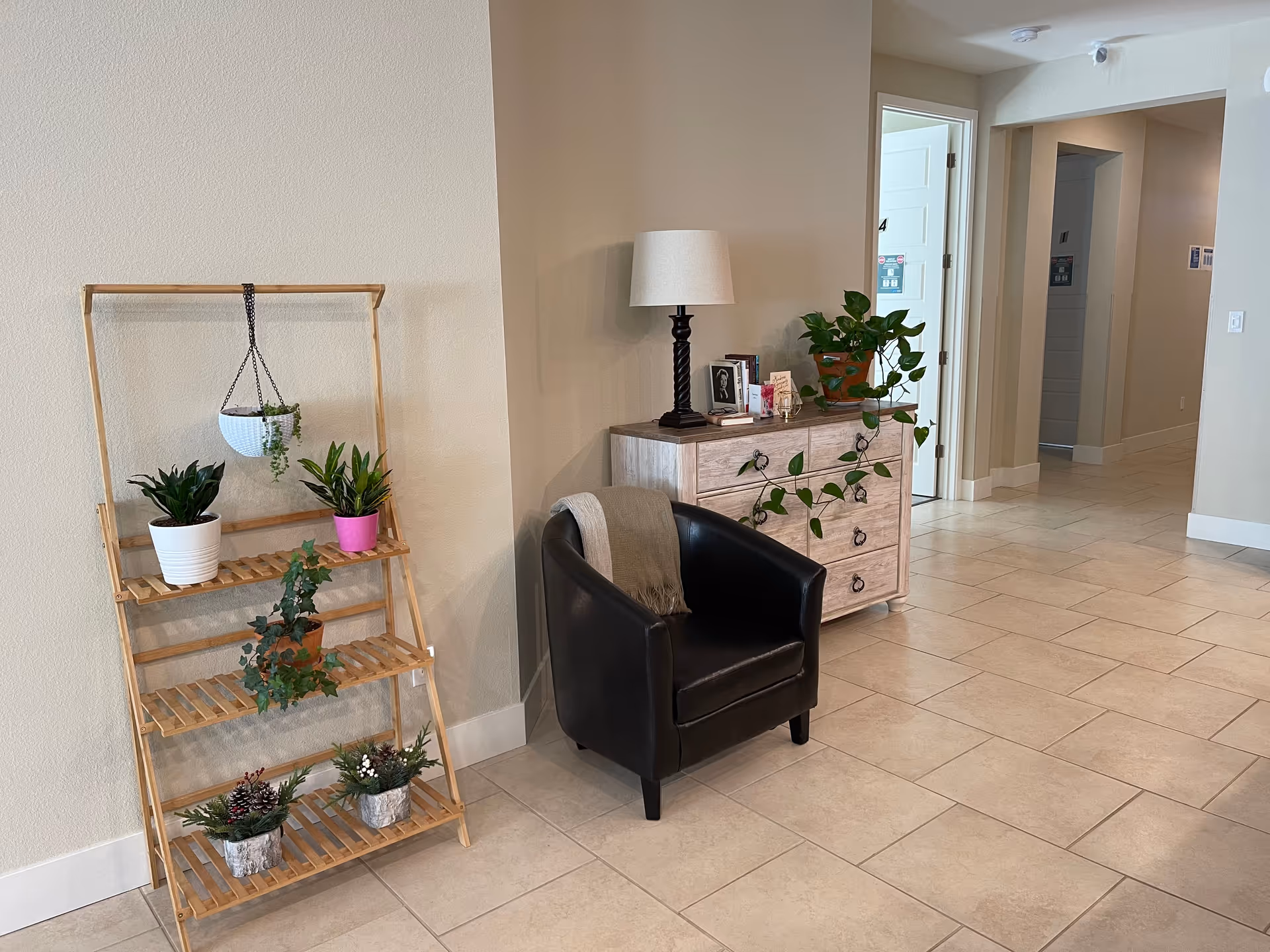 A quiet lobby corner with a black armchair, wooden chest, and potted plants.
