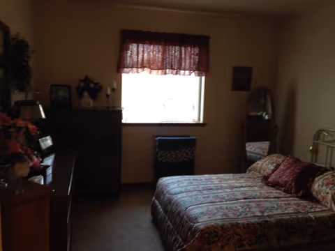 Floral-patterned bedroom with a bed, dresser, and window in a cozy, sunlit room.
