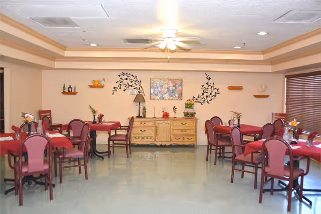 A dining room with red tablecloths, purple chairs, and a sideboard under wall art.