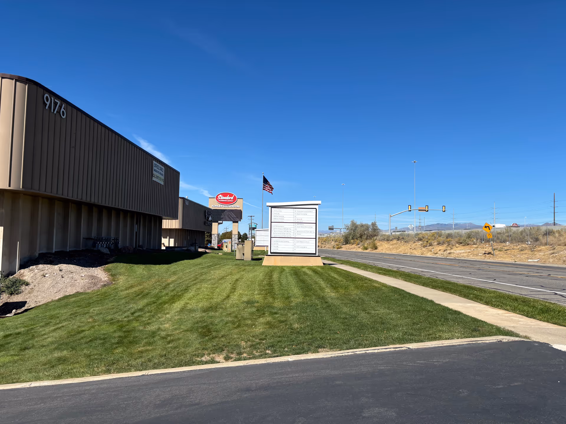 Exterior view of a beige building by the road with a sign and flag.