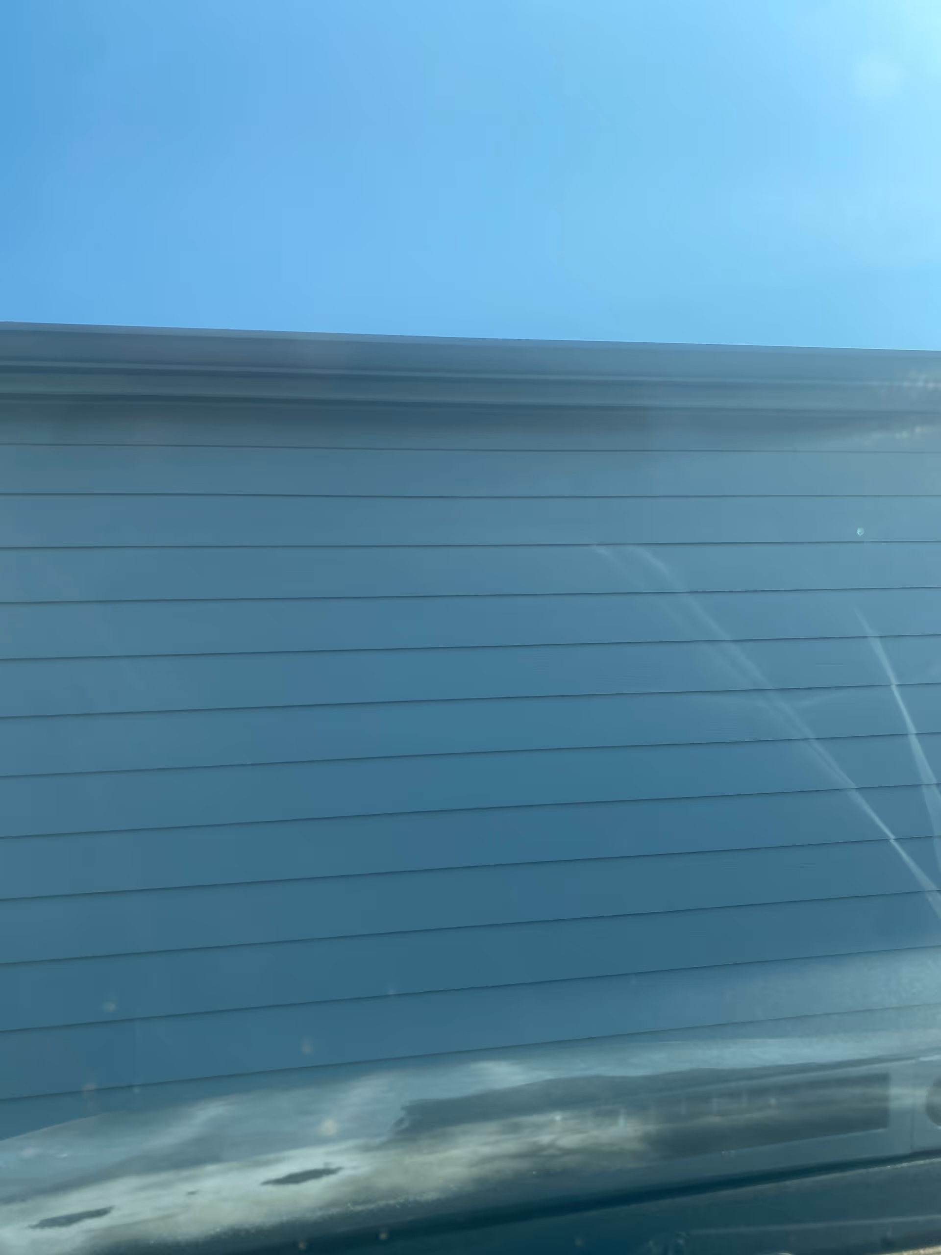Blue sky above a blue exterior wall with horizontal siding.