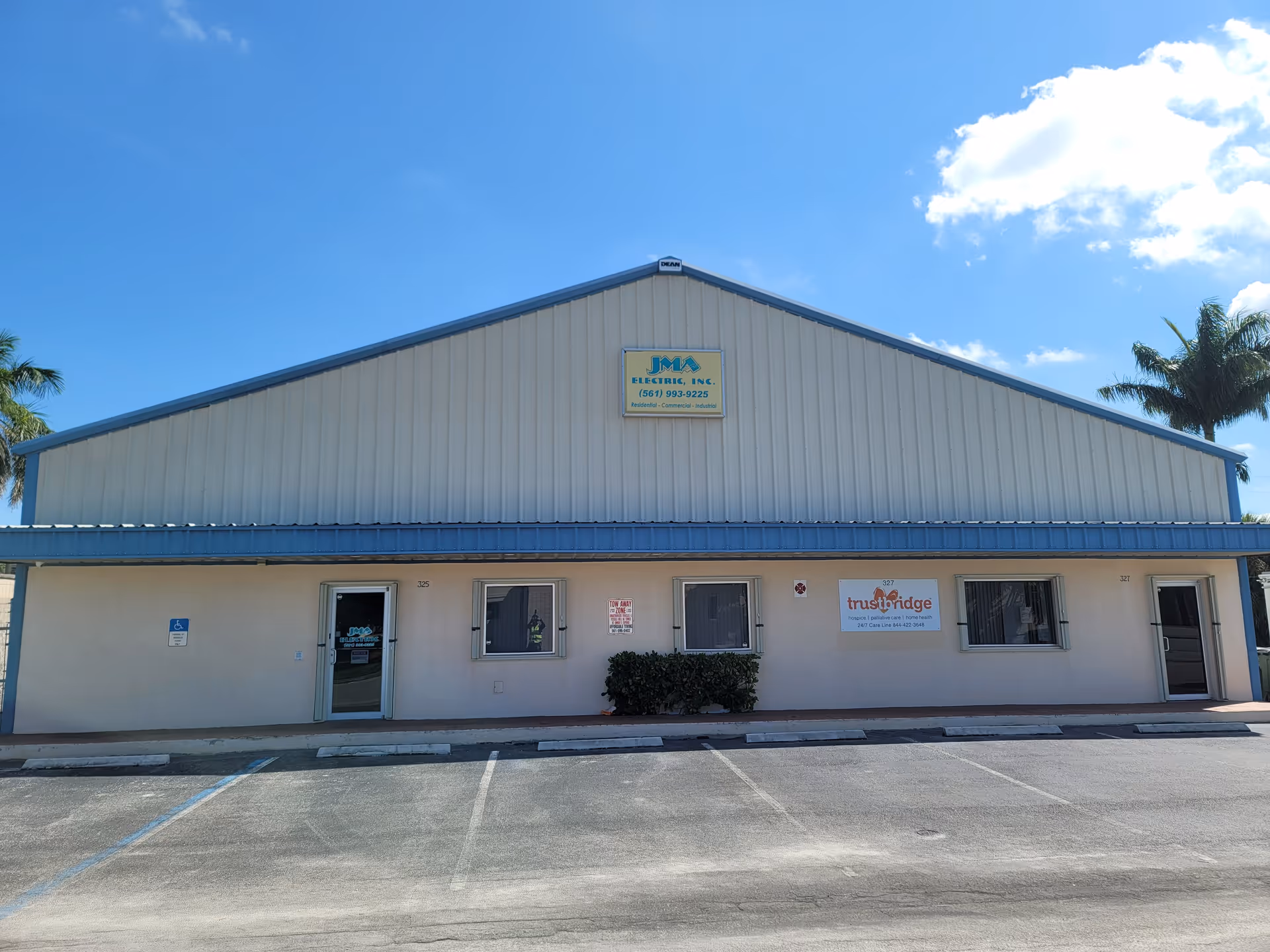 Front view of Trustbridge Belle Glade, a beige, single-story senior facility with a blue roof.