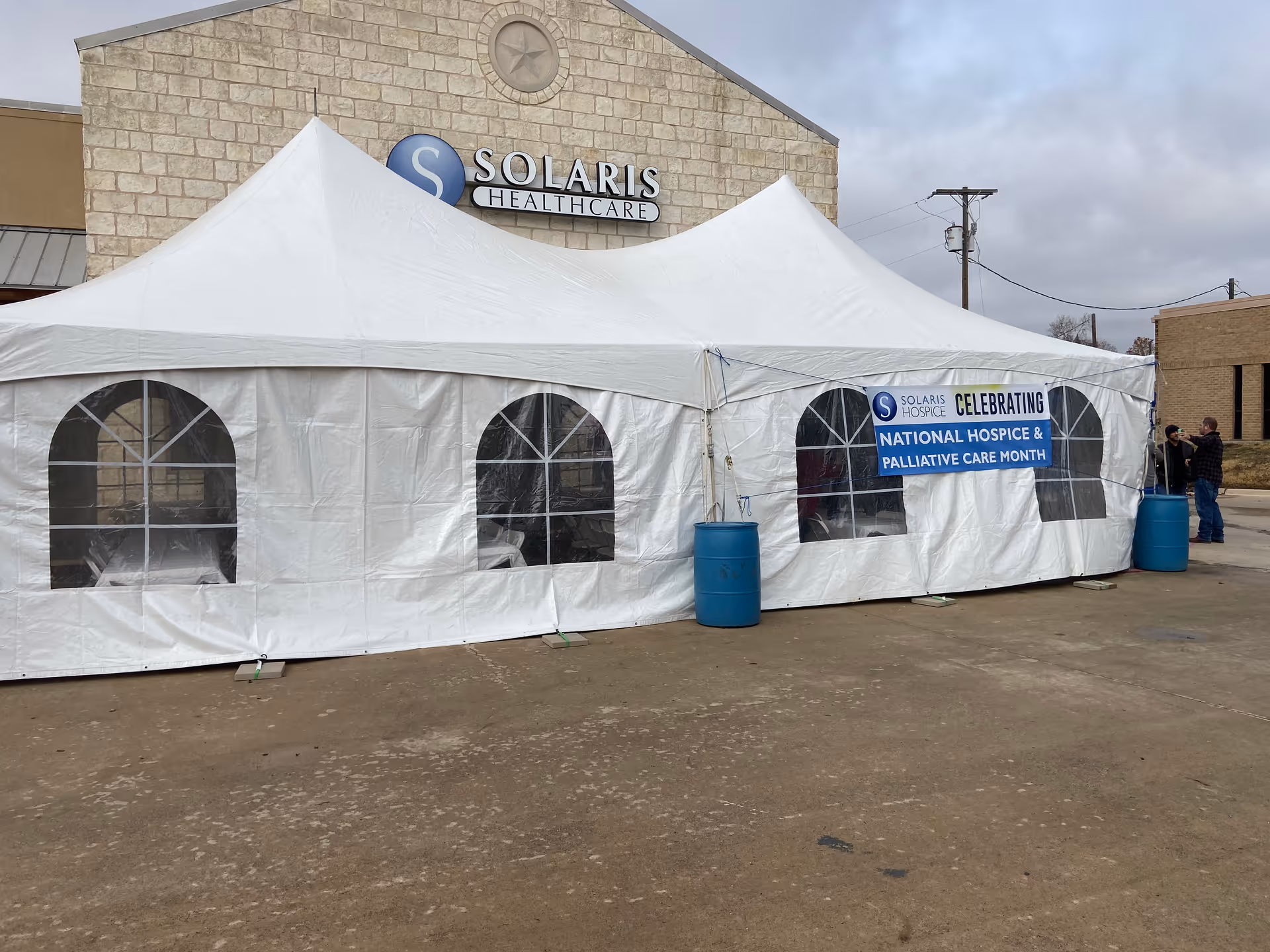 A white event tent is set up outside Solaris Healthcare with banners and blue barrels.