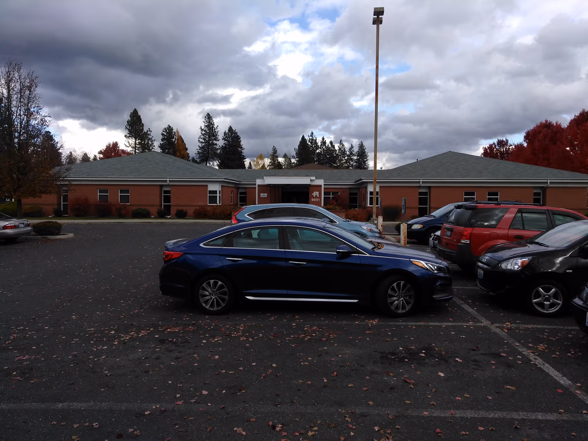 Front exterior of a brick senior care facility with parked cars.