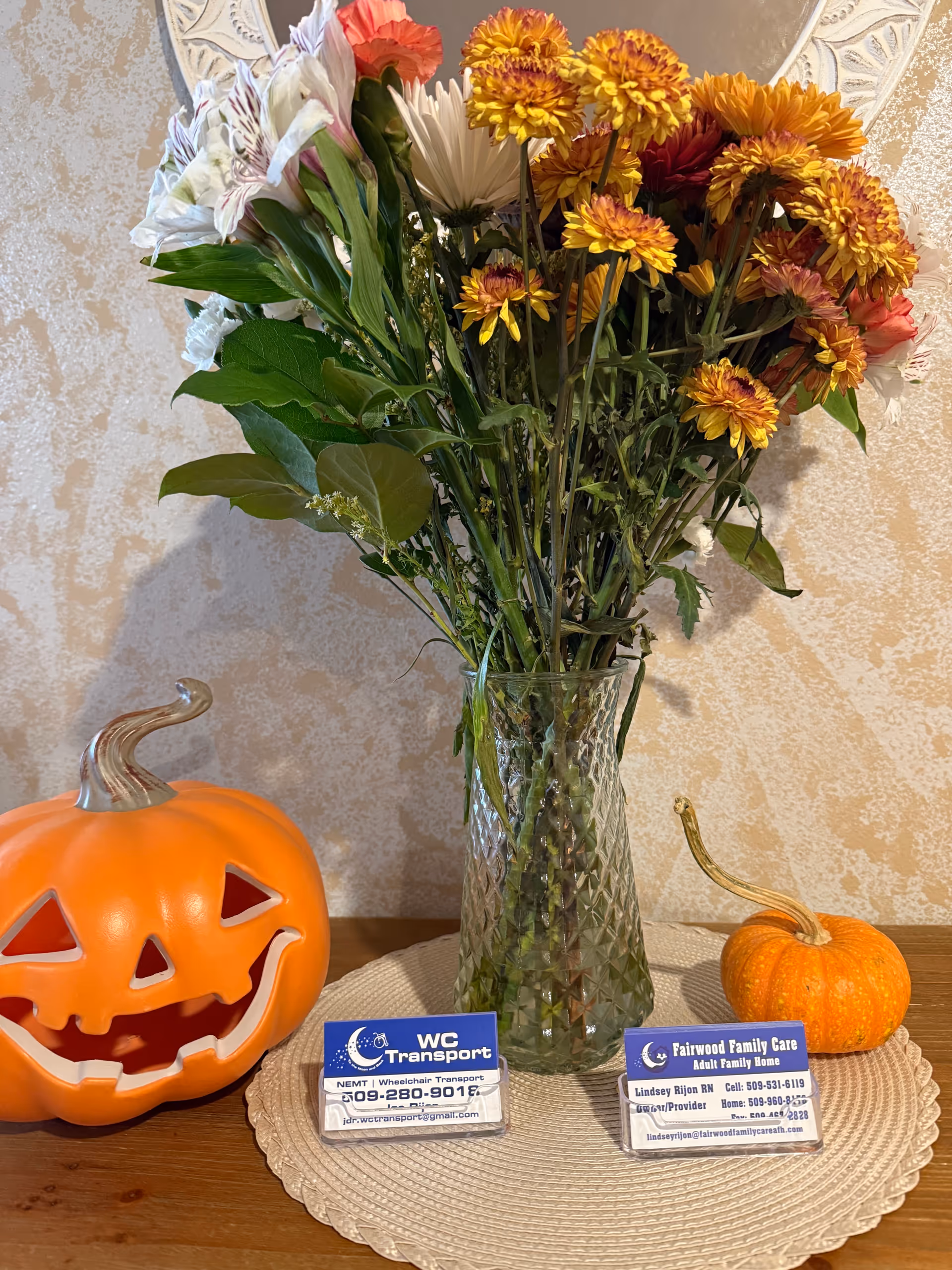 A vase of flowers with two pumpkins and business cards on a table.