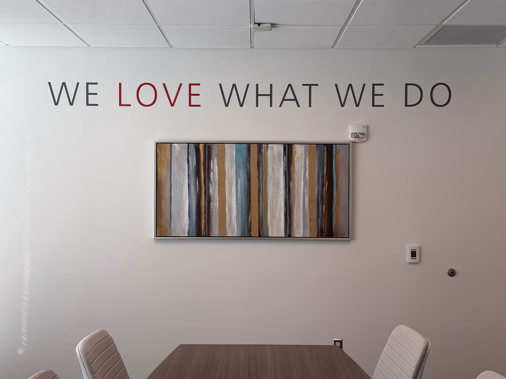 Modern interior with wall slogan WE LOVE WHAT WE DO and abstract artwork above a table.