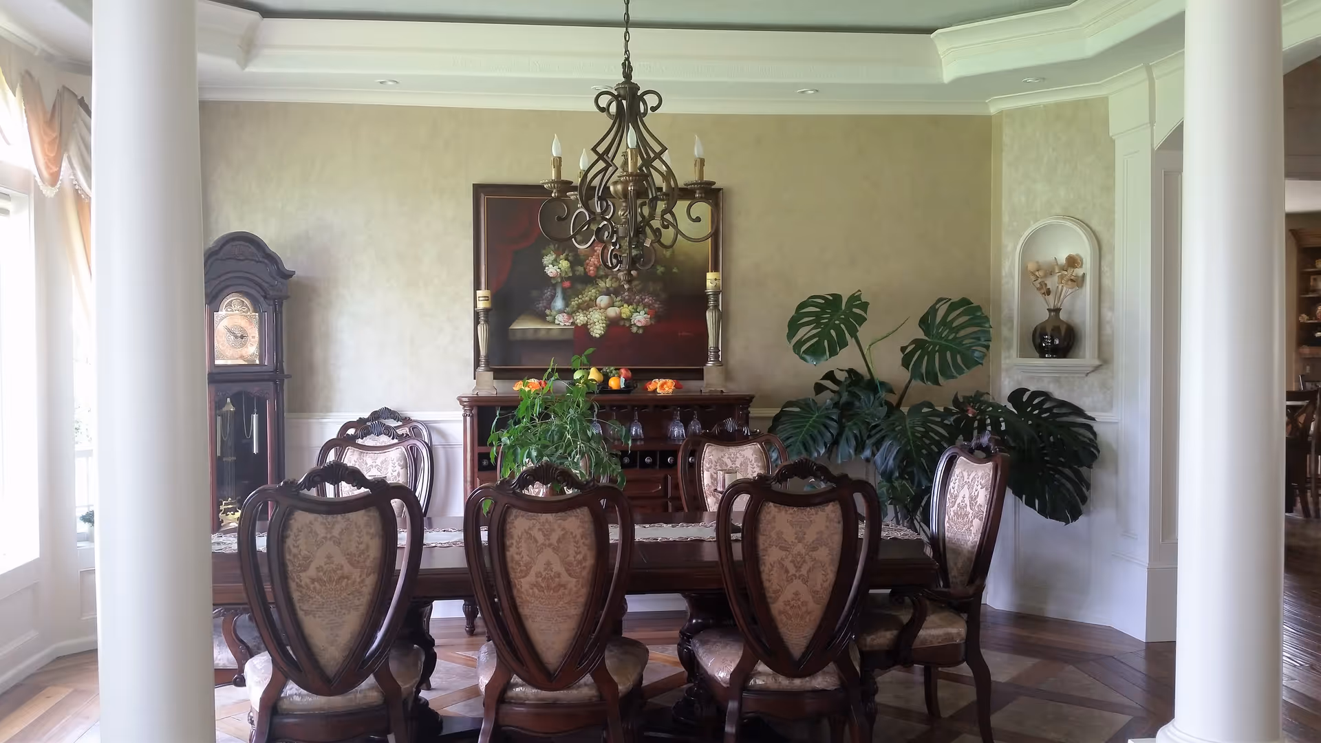 Elegant dining room with ornate chairs, chandelier, plants, and a long table.