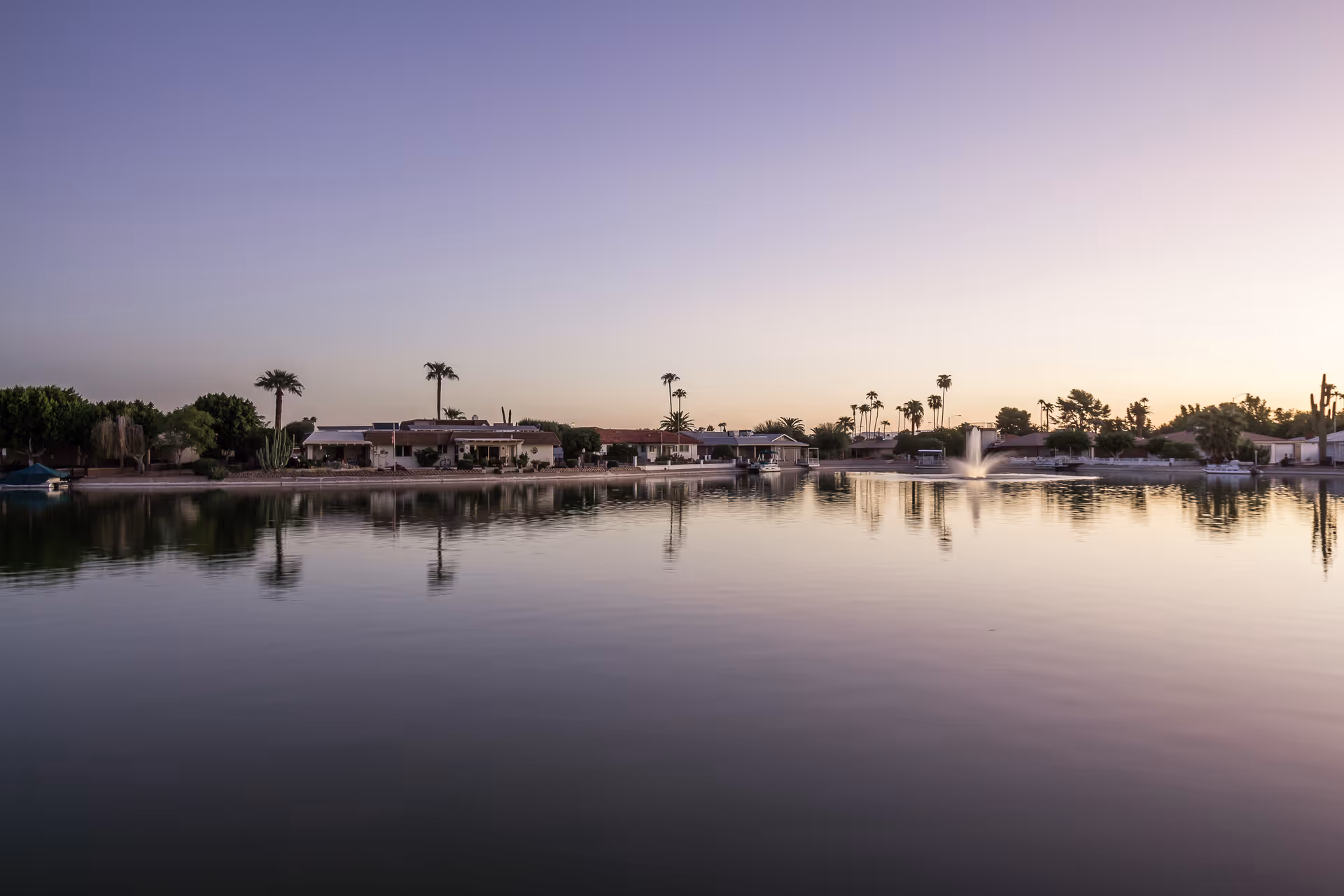 Sunset over a lakeside senior living community with palm trees and low-rise buildings.