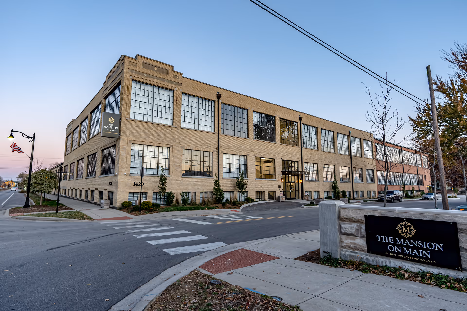 Street view of The Mansion on Main, a large brick building with many industrial-style windows and a front sign by the sidewalk.