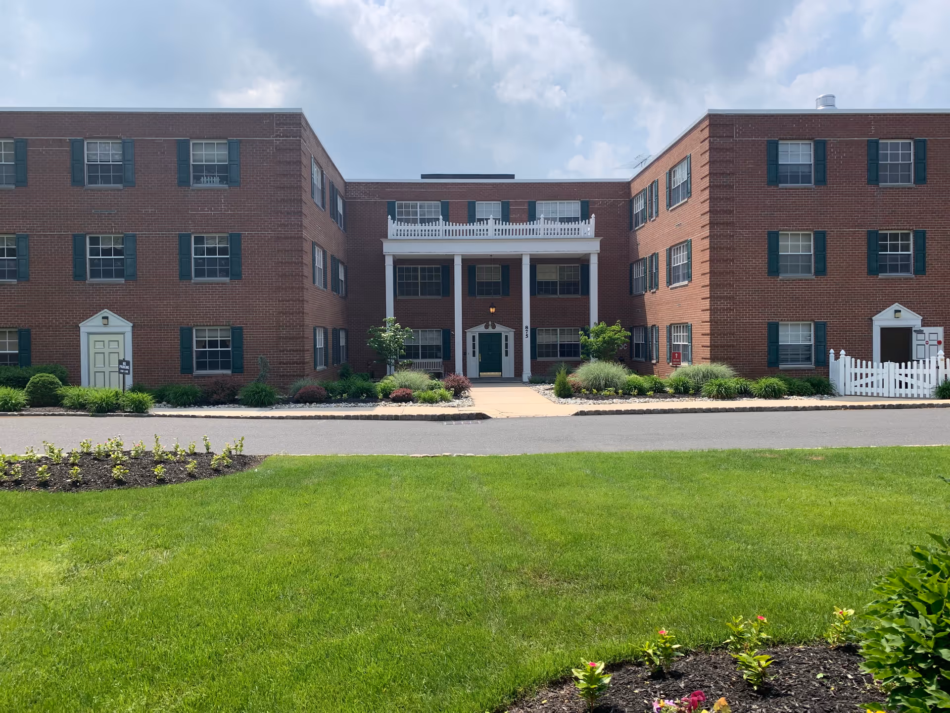 Brick senior living facility exterior with central entrance, white columns, and landscaped grounds.