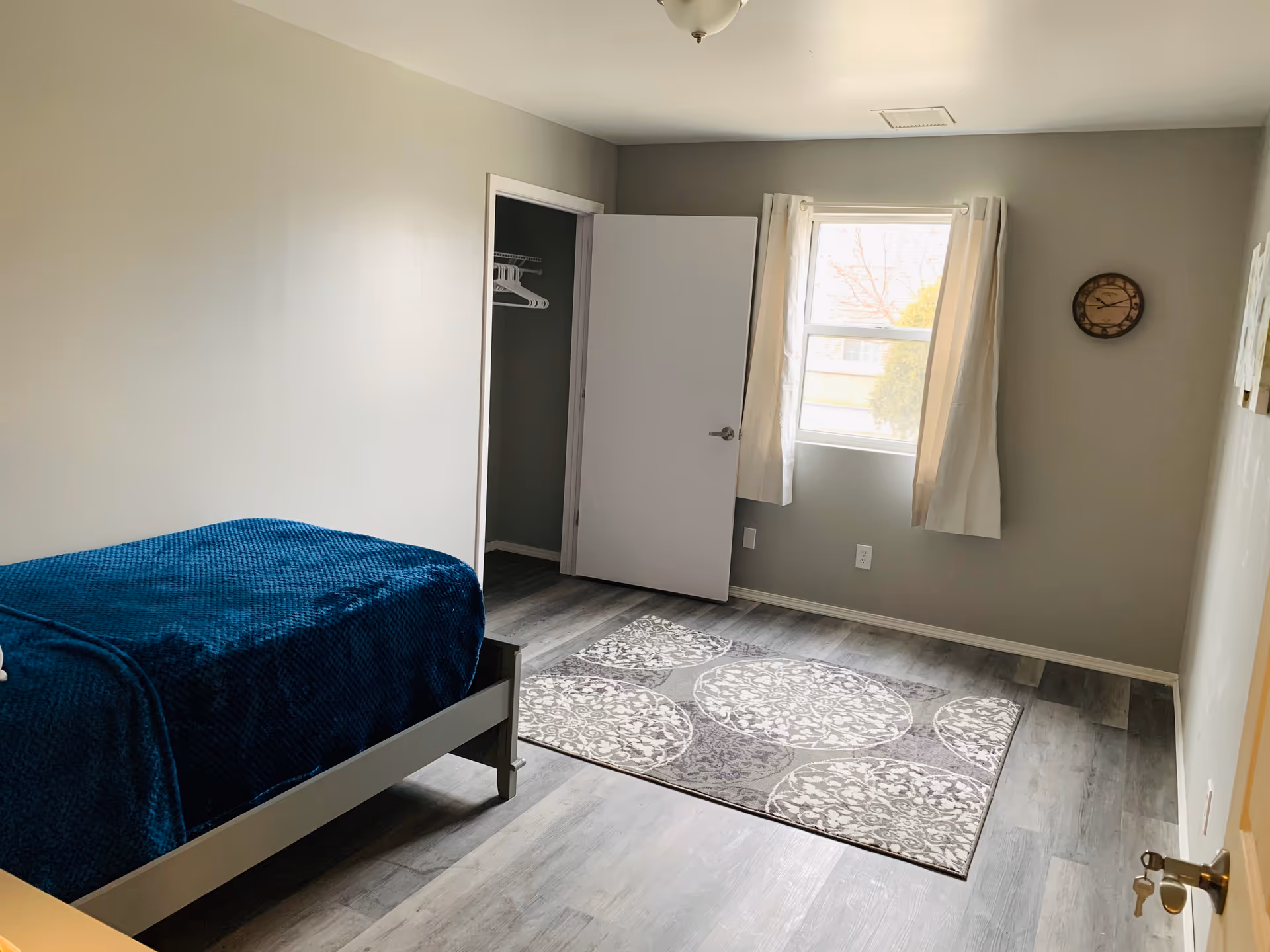 A small Hartford Estates bedroom with a bed, open closet, window, curtains, and rug.
