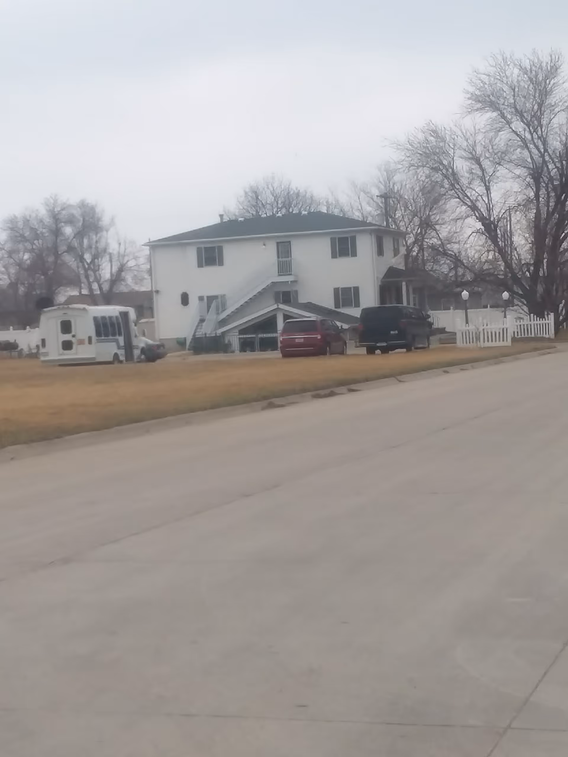 Exterior view of Champion Homes of Hastings: two-story white building with stairs, fence, and parked vehicles.
